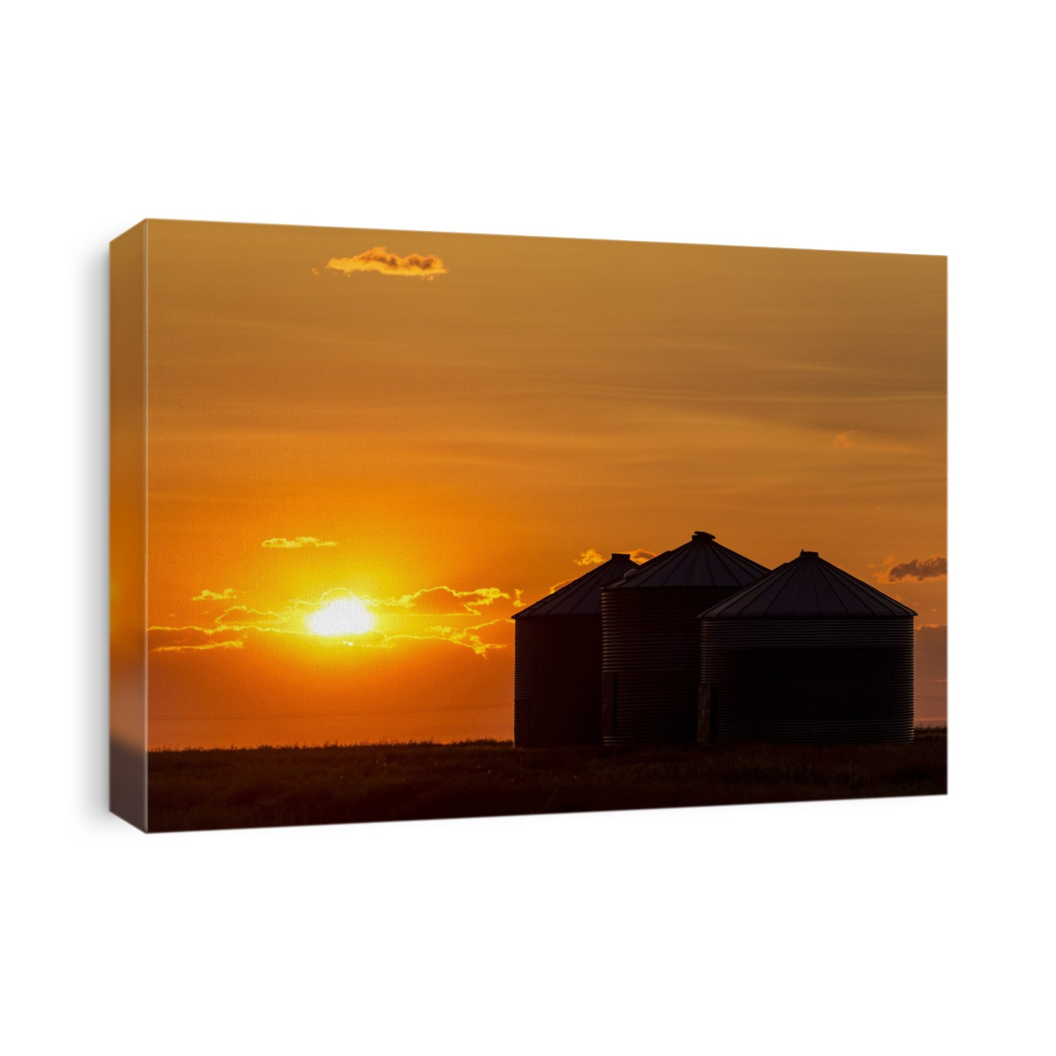 Silhouette of large metal grain bins at sunrise with orange sun rising over clouds; Alberta, Canada