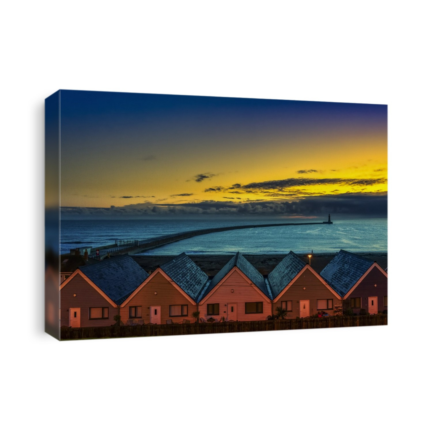 Row of illuminated houses at Roker Beach in Sunderland with a silhouette of the  Roker Lighthouse in the distance at the end of the pier and long breakwater jutting out from the shore at sunset; Sunderland, Tyne And Wear, England, United Kingdom