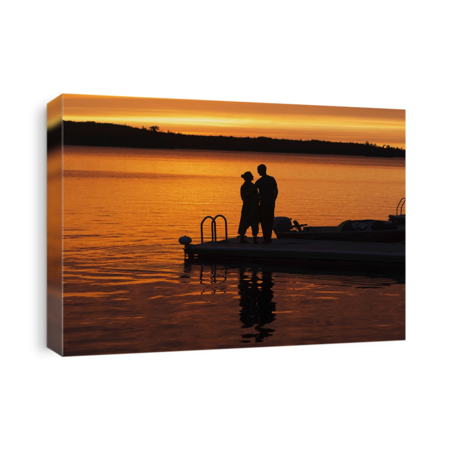 Silhouette Of A Couple Standing At The End Of A Dock At Sunset With An Orange Glow In The Sky And Reflected In The Tranquil Lake Water; Ontario, Canada