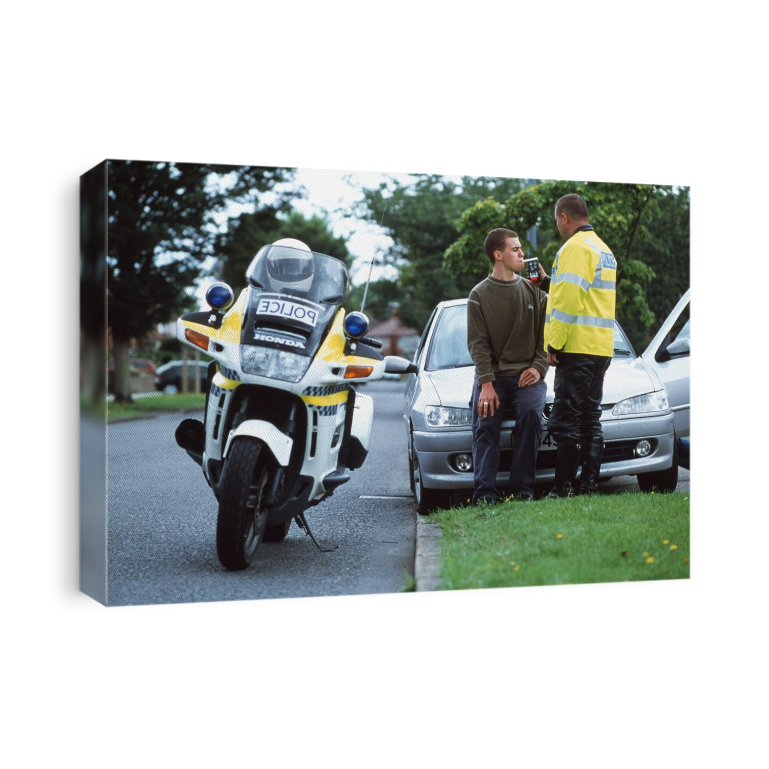 Alcohol breath test. Policeman breathalyzing a motorist by his car at the side of a road. He is suspected of illegally driving while under the influence of alcohol (drink-driving).