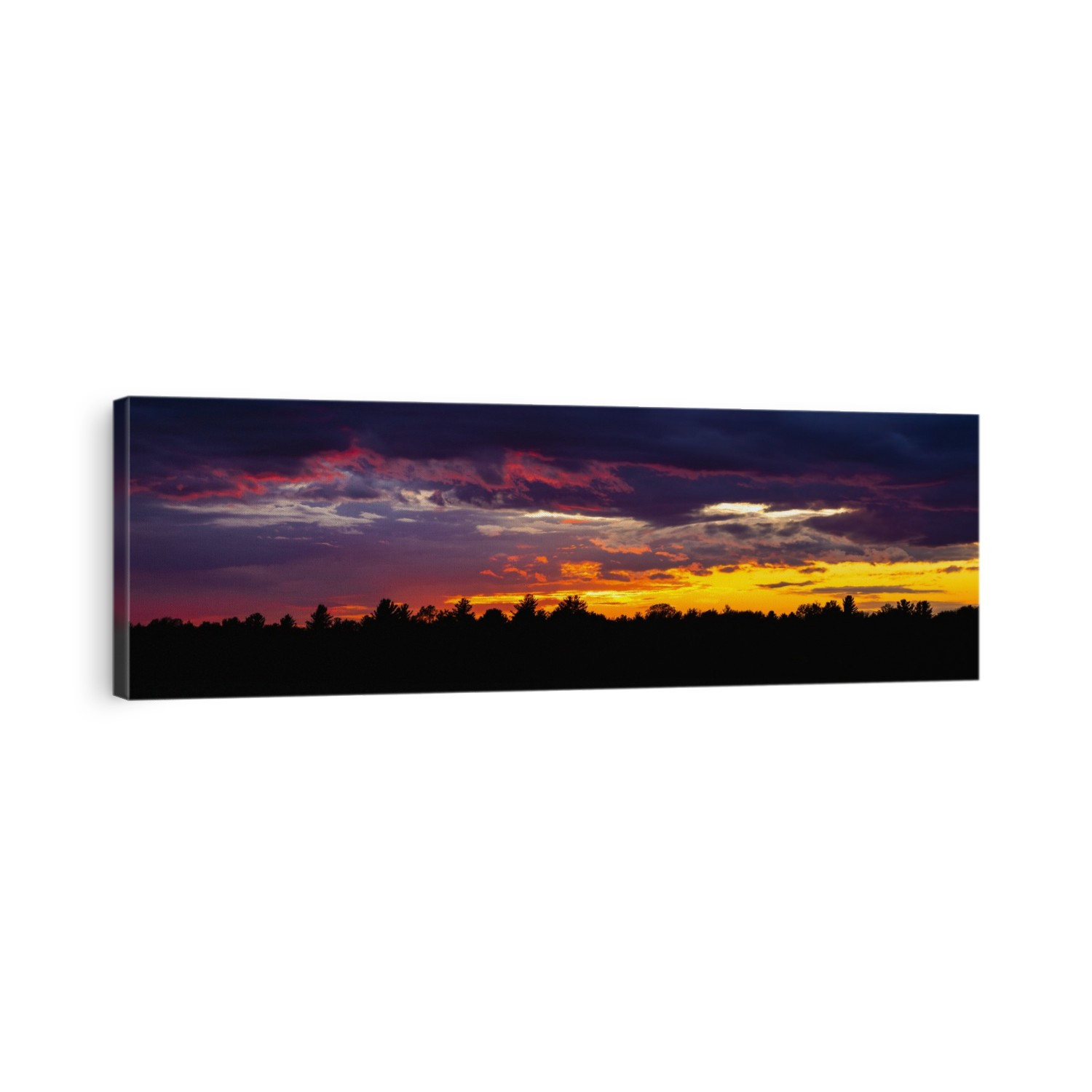 Dramatic sky at sunset with dark clouds and colourful light glowing above silhouetted trees; Bromont, Quebec, Canada