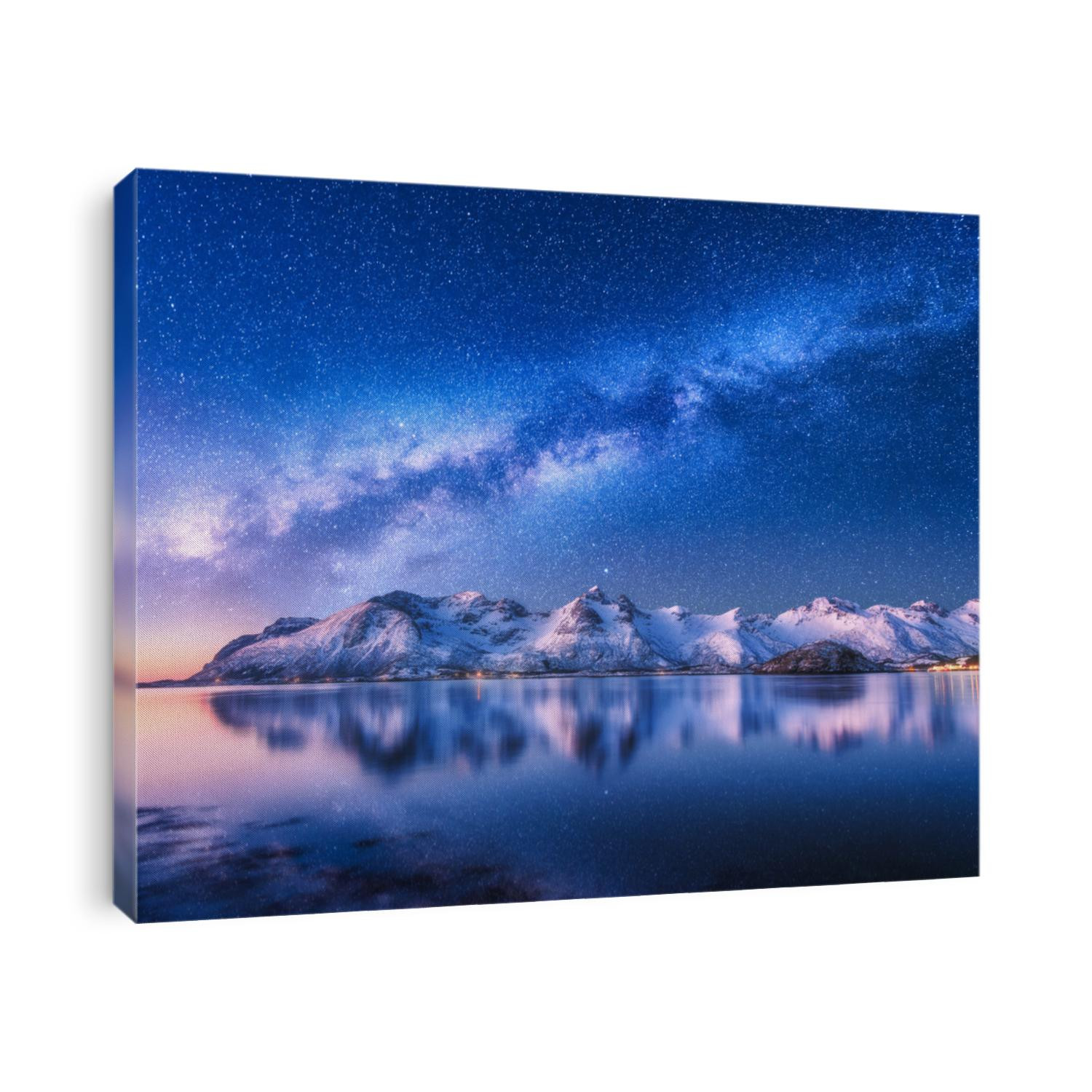 Bright Milky Way over snow covered mountains and sea at night in winter in Norway. Landscape with snowy rocks, starry sky, reflection in water, fjord. Lofoten Islands. Space. Beautiful milky way