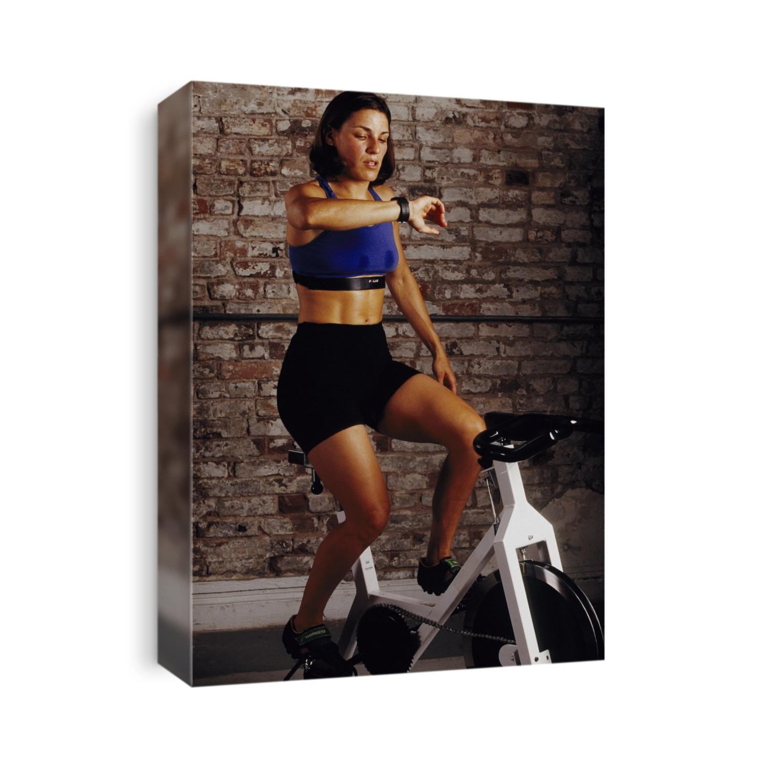 Young woman exercising on a stationary bike checking her heart rate.