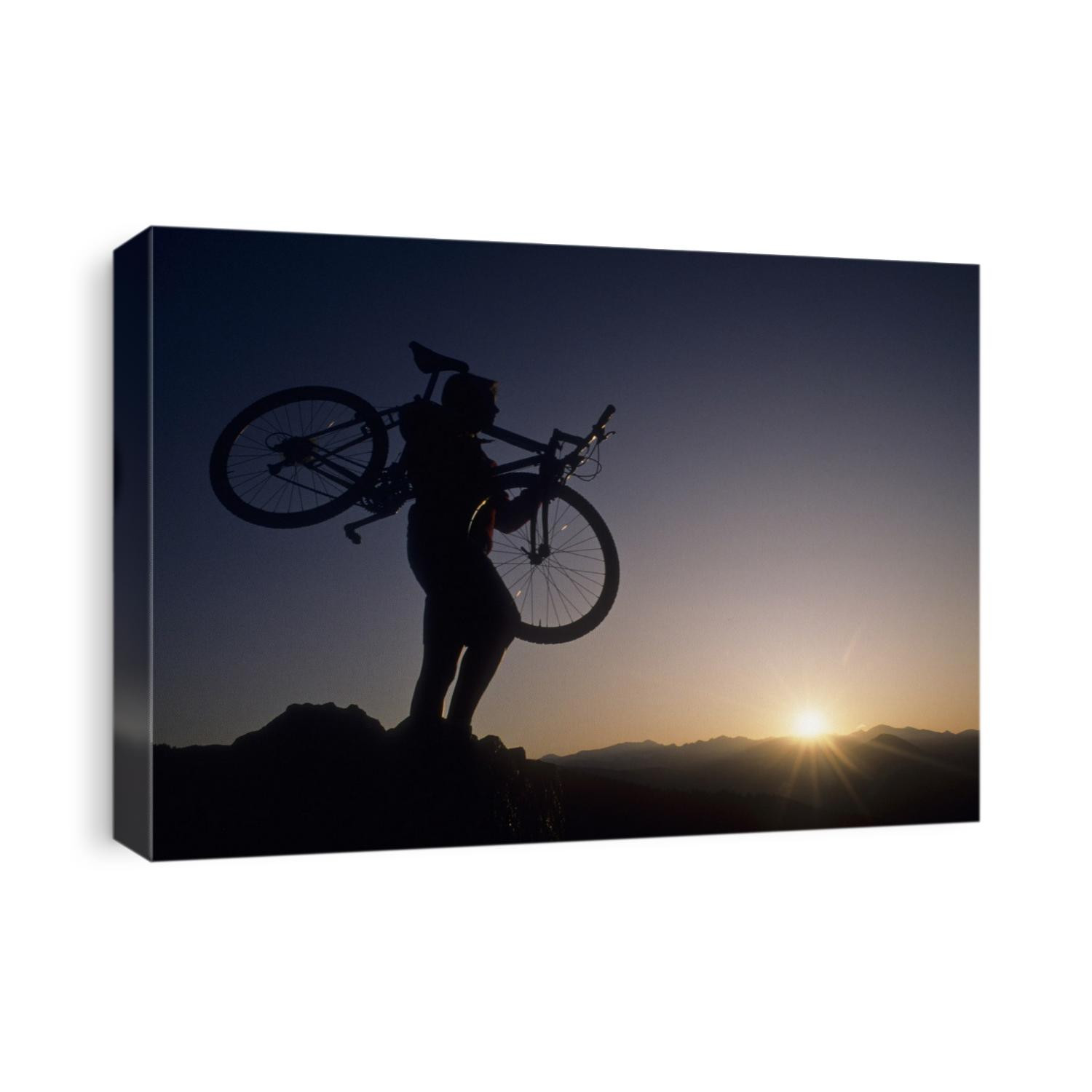 Silhouette of mountain biker at the summit during sunrise.