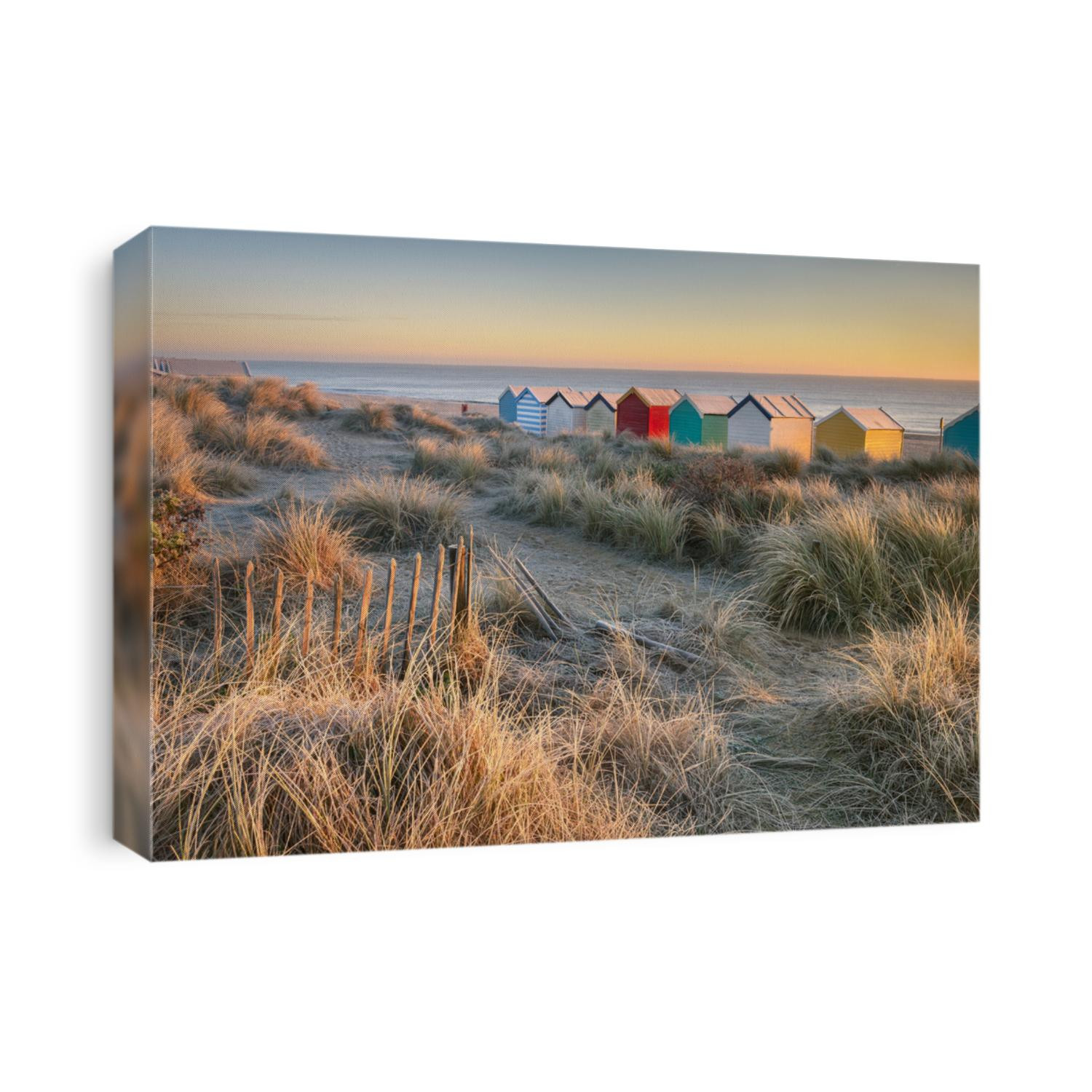 The warm dawn sun light hits the cold and frosty dunes behind the colourful beach huts on Southwold Beach.