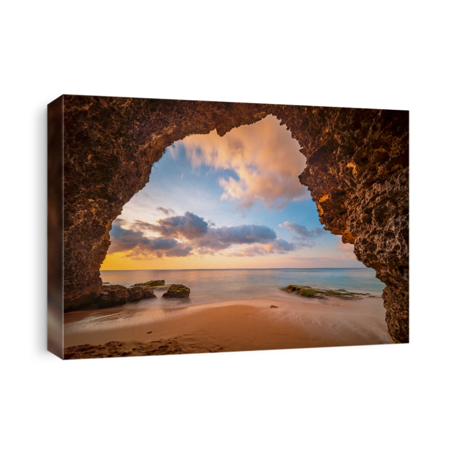 View from the cave a sandy beach along the ocean at golden sunset. Bali, Indonesia.