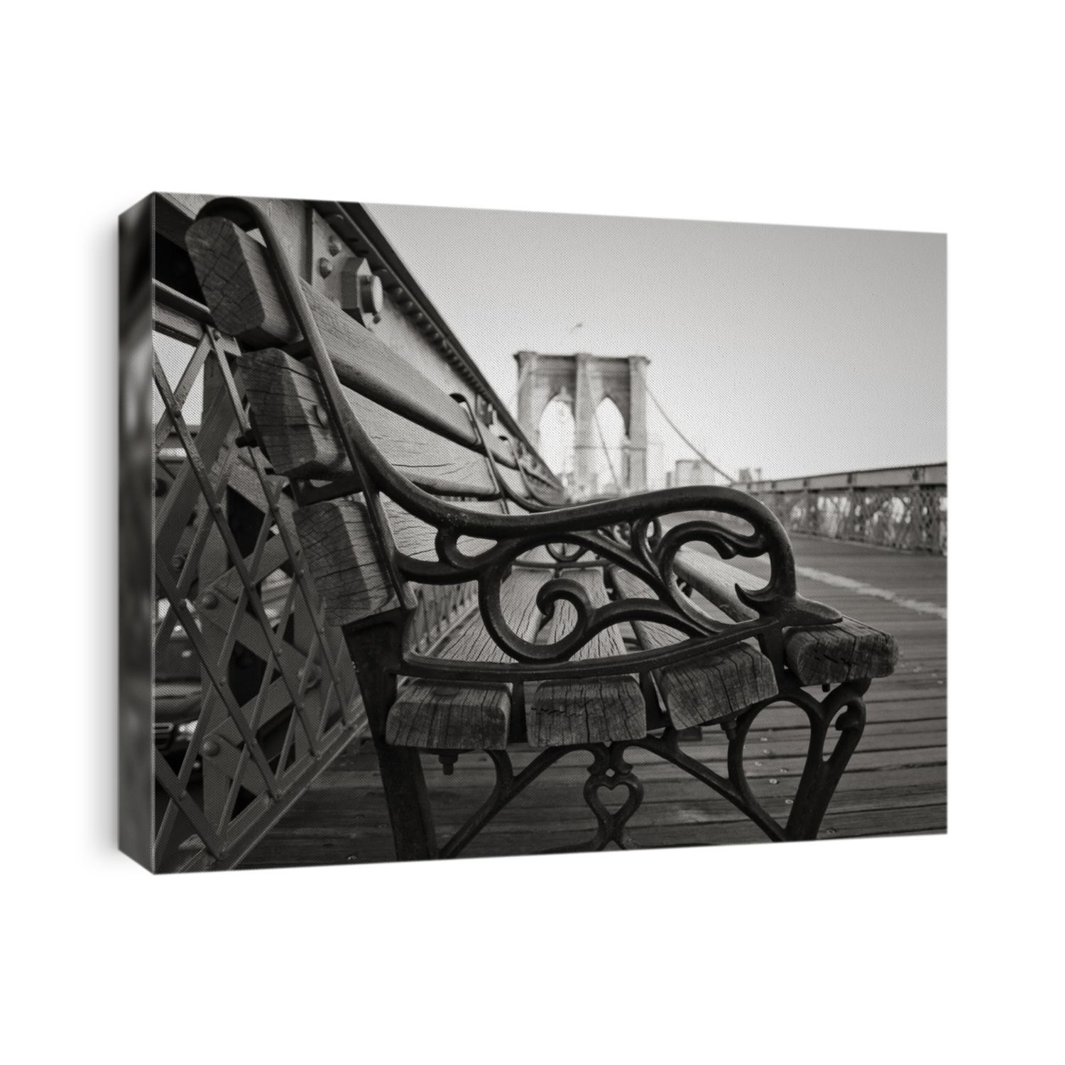 A vintage park bench on the Brooklyn Bridge facing Manhattan in black and white.